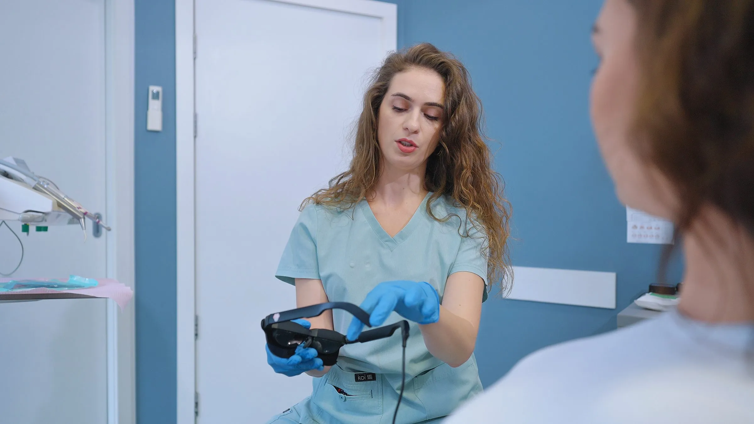 Lekarka w rękawiczkach pokazuje pacjentce okulary Dental Glasses i wyjaśnia, jak działają